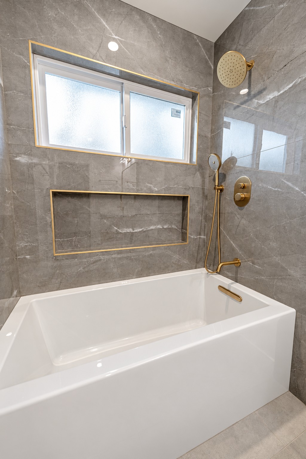 Bathroom with gray stone tile, white bathtub and gold fixtures